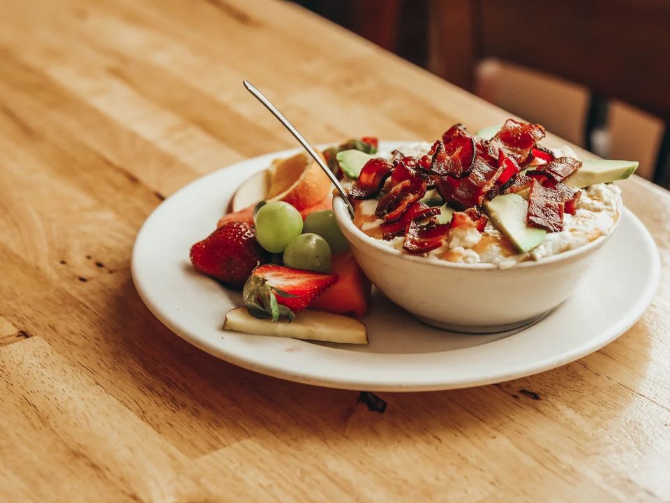 A bowl of oatmeal topped with bacon and a plate of fresh fruit