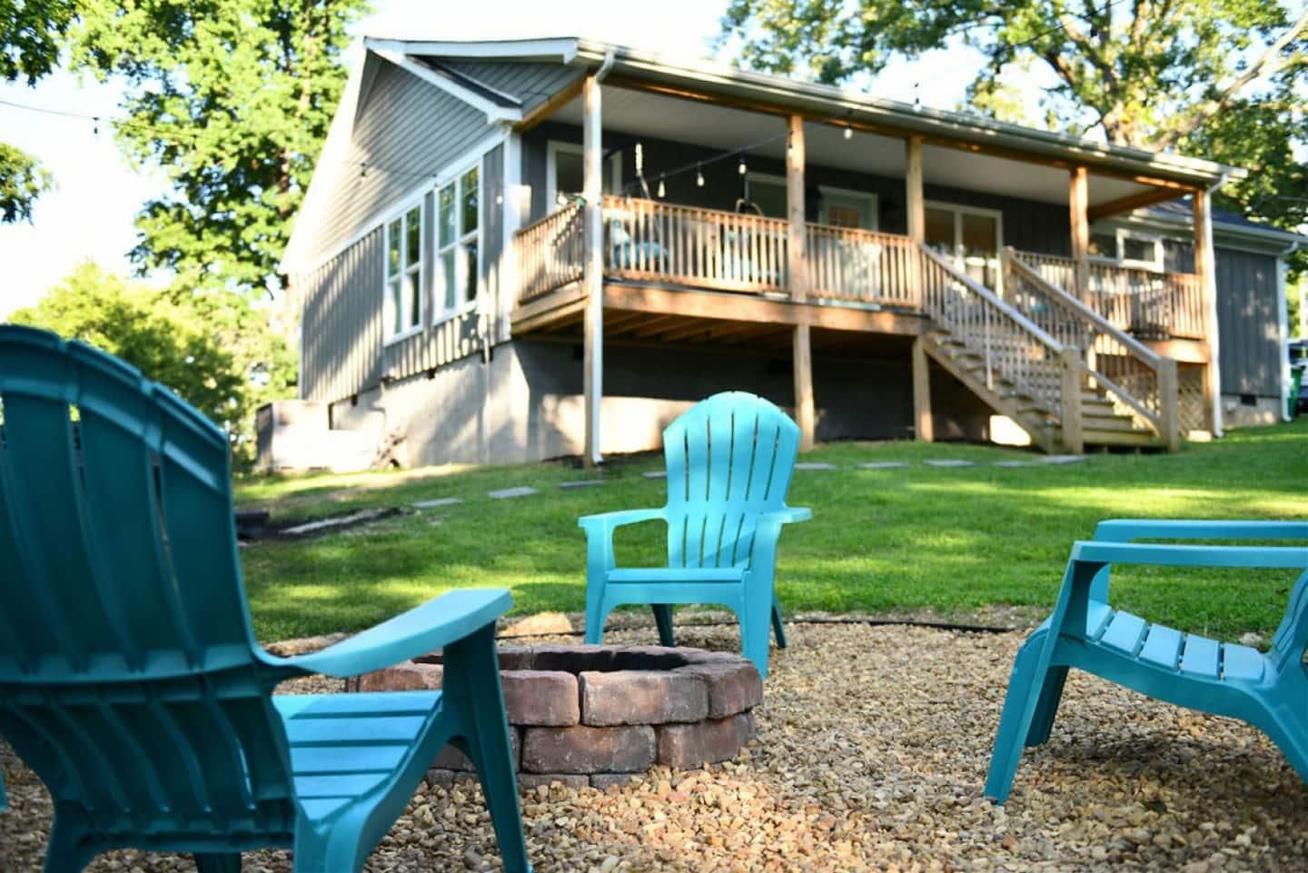 Teal chairs around the stone fire pit with the house behind