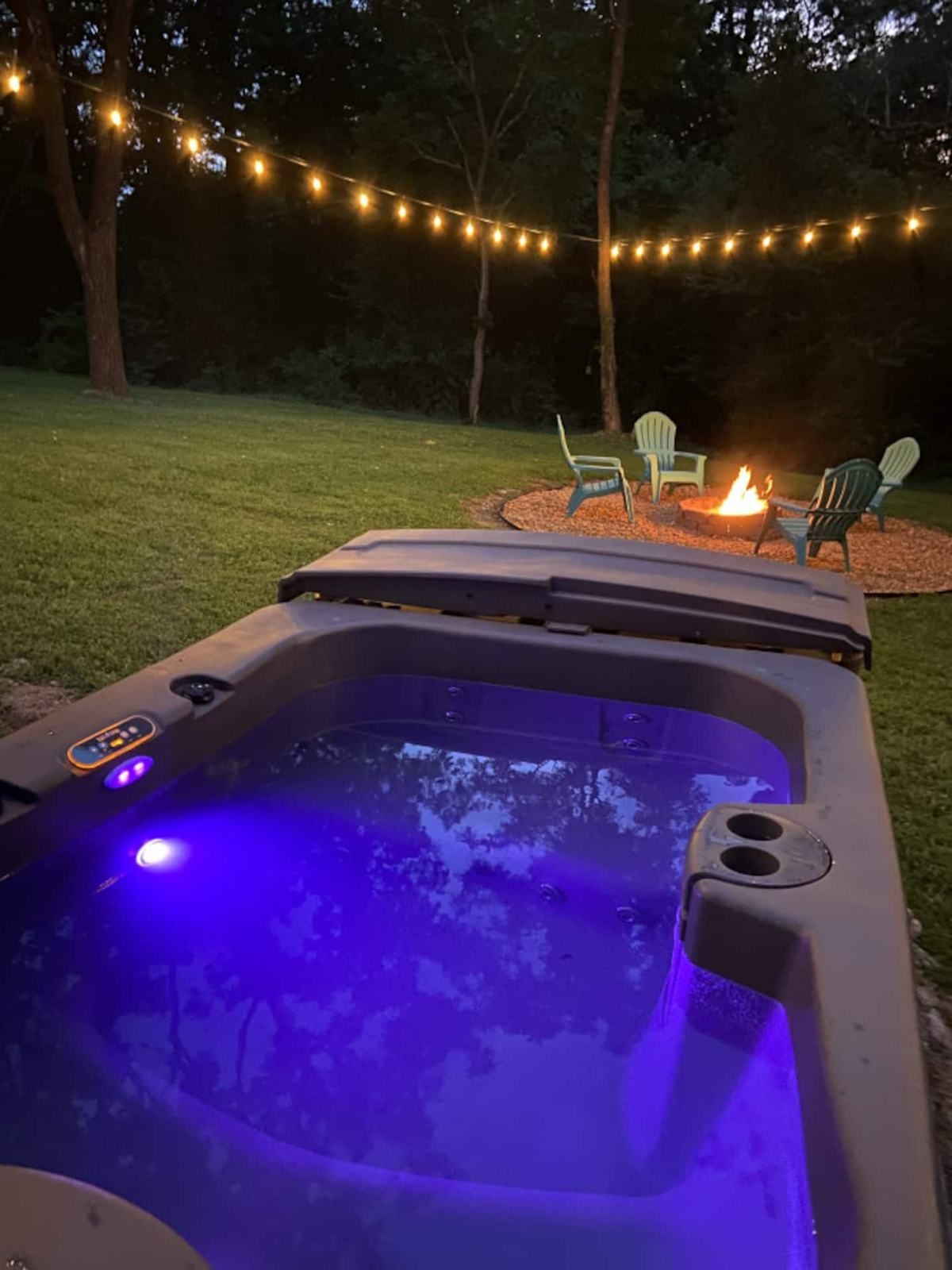 The hot tub lit up at night with the fire pit glowing behind it
