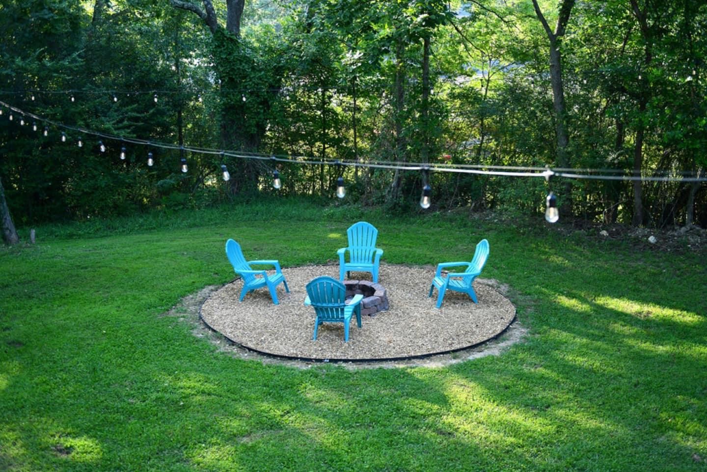 String lights strung over the gravel fire pit circle and teal Adirondack chairs