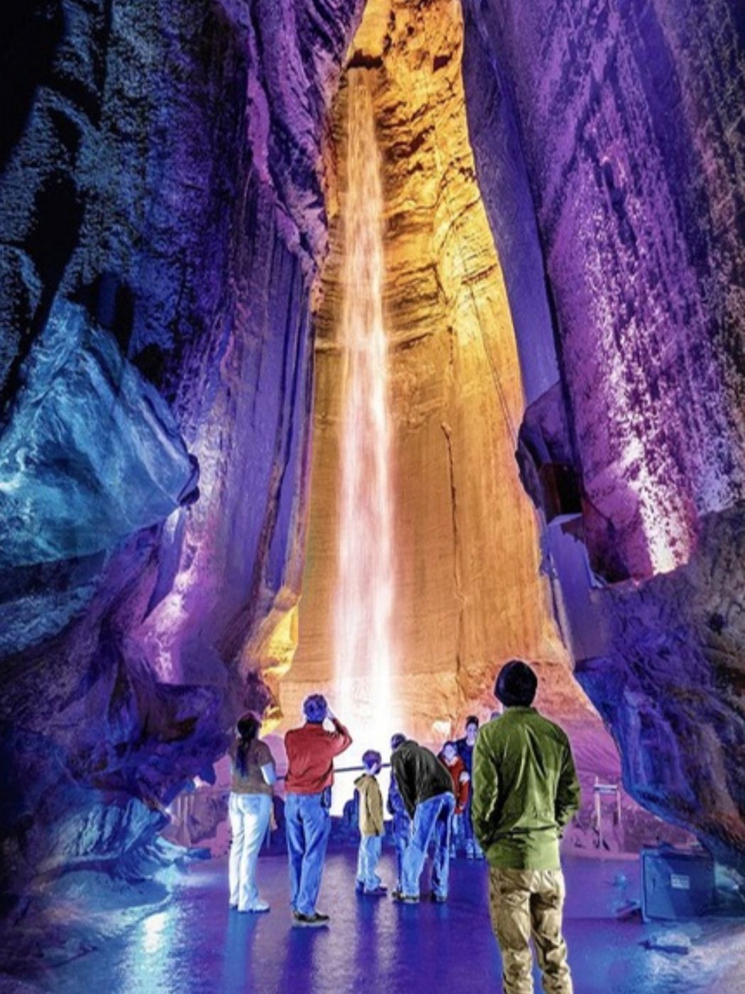 Visitors looking up at Ruby Falls lit in purple and gold inside the cave