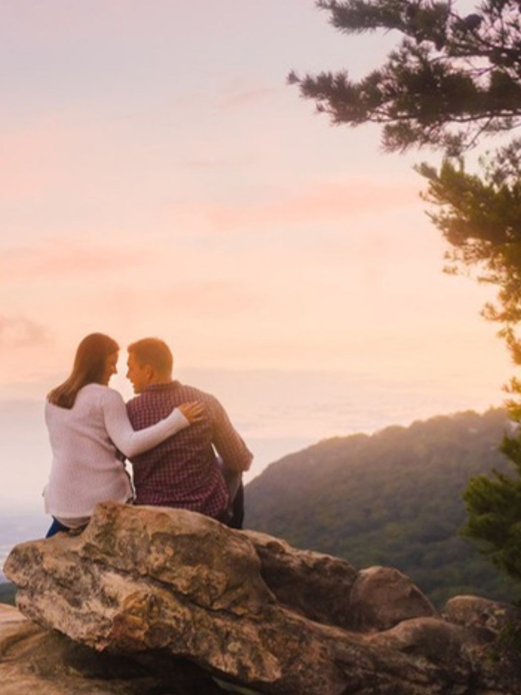 A couple sitting on a rock ledge above the valley at sunset