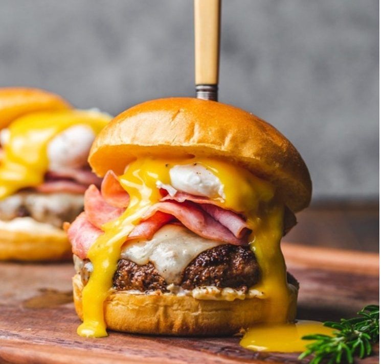 A tall burger with ham and melting cheese